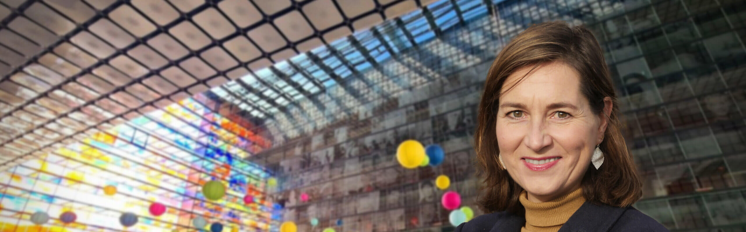 Lächelnde Ulrike Nagel mit braunem Haar vor dem bunten Glasdach des Museums Beeld en Geluid in Hilversum