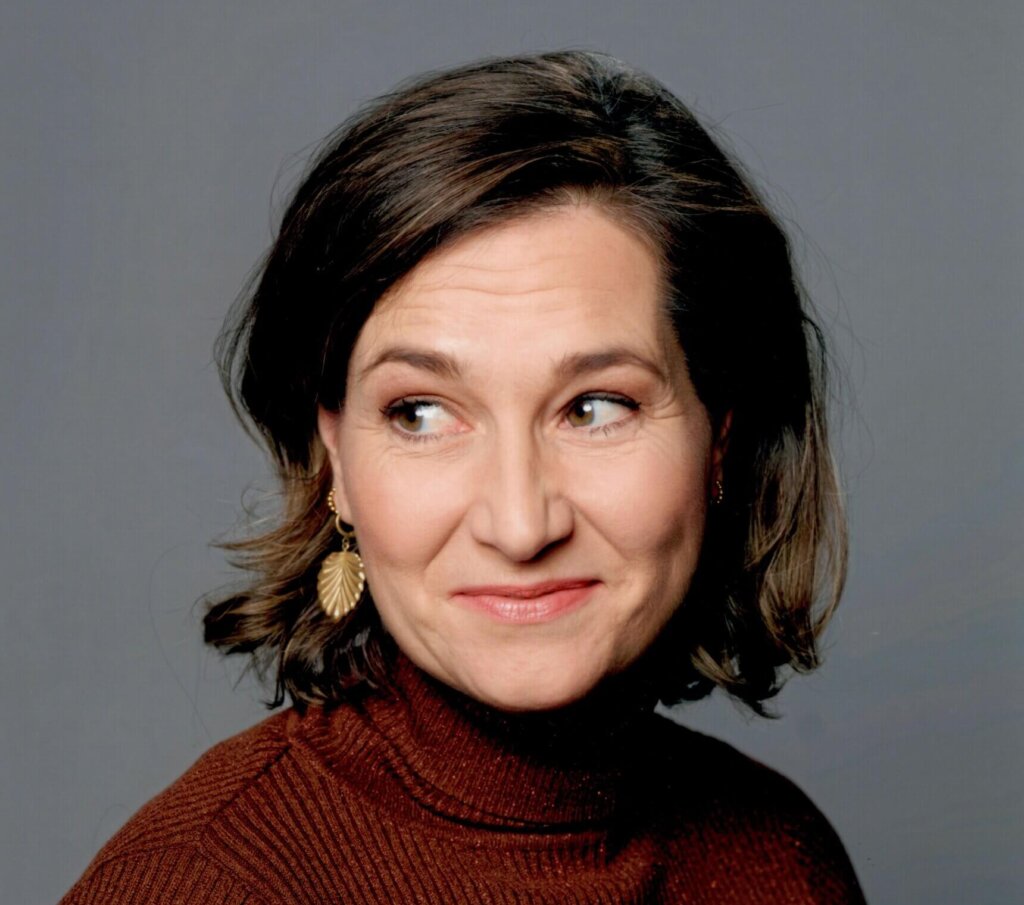 Portretfoto van een Ulrike Nagel met donker haar, gouden oorbellen en een bordeauxrode coltrui
